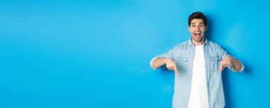 Heyecanlı yakışıklı bir adamın mavi arka plana karşı durarak bir duyuru yaptığı görüntüsü..