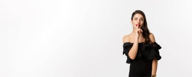 Moda ve güzellik. Siyah elbiseli, kırmızı dudaklı, kameraya göz kırpan, beyaz arka planda duran, sessiz bir kadın..