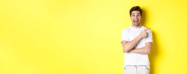 Heyecanlı gülümseyen bir adam resmi. Kara Cuma teklifleri sunuyor, parmağıyla işaret ediyor ve şaşırmış görünüyor. Sarı arka planda duruyor..