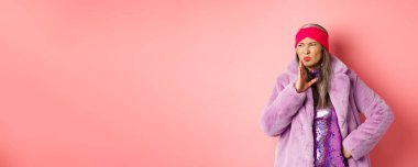 Moda ve alışveriş konsepti. Şık, orta yaşlı, şık kışlık giysiler içinde zarif bir Asyalı kadın kötü bir koku alıyor. İğrenç kokulu pembe arka planda el sallıyor..