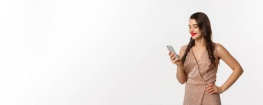 Noel partisi ve kutlama konsepti. Telefonla mesaj okuyan, gülümseyen, akıllı telefon kullanan, lüks elbiseler giyen, beyaz arka planda yaşayan mutlu genç bir kadın..