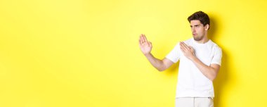 Kung-fu yetenekleri olan bir adam, dövüş sanatları ninja hareketi, beyaz tişörtler içinde dövüşmeye hazır, sarı arka planda duruyor..