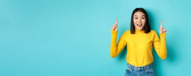 Alışveriş konsepti. Etkilenmiş genç Koreli kadın üzerinde reklam gösteriyor, parmaklarını havaya kaldırıyor ve hayrete düşüyor, 