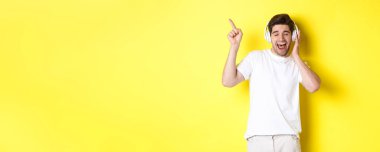 Kulaklıkla müzik dinleyen mutlu adam, siyah cuma için tanıtım teklifini işaret ediyor, sarı arka planda duruyor..