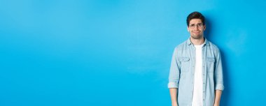 Gözlüklü şüpheli ve şüpheli bir adam. Tuhaf, mavi arka planda bir şeye bakıyor..