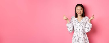 Koreli kalp işaretleri gösteren, gülümseyen, romantik pembe arka planda duran Asyalı güzel bir kadın..