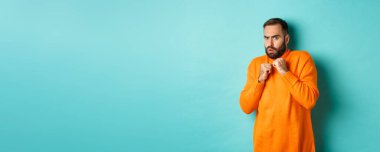 Korkak adam ürktü, korkutucu bir şeye bakıyordu, turuncu süveter içinde, stüdyo arka planında duruyordu..