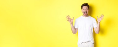 Heyecanlı ve şaşırmış bir adamın portresi büyük reklam teklifine tepki veriyor, sevinç ve zafer için bağırıyor, sarı arka planda duruyor..