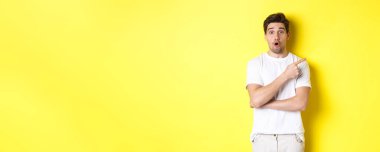 Şaşırmış yakışıklı adamın portresi sağ eli işaret ediyor, hayret içinde, sarı arka planda duruyor..