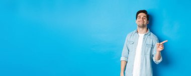 Kendine güveni tam olan yakışıklı adam küstah, parmağını fotokopi alanına doğrultuyor, reklamını yapıyor, mavi arka planda duruyor..