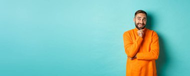 Düşünceli sakallı adam seçim yapıyor, alışveriş yapıyor ve sol üst köşeye bakıyor, tatmin olmuş gülümsüyor, turkuaz arka planda duruyor..