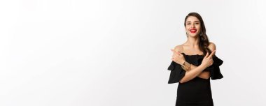 Moda ve güzellik. Güzel, mutlu bir kadın iki seçenek gösteriyor, gülümsüyor, siyah elbise giyiyor, beyaz arka plan..