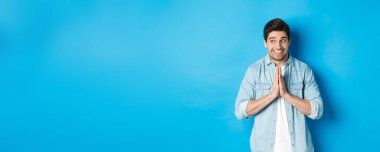 Umut dolu gülümseyen adam sola bakıyor, el ele tutuşup dua ediyor, bir şey dileniyor ya da yalvarıyor, mavi arka plana karşı duruyor..