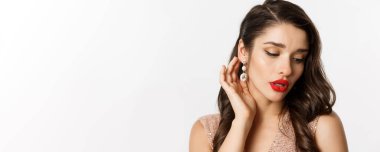 Yeni yıl kutlaması ve kış tatili kavramı. Kırmızı dudaklı zarif esmer kadının portresi, küpeler gösteriyor ve şehvetli görünüyor, beyaz arka plan..