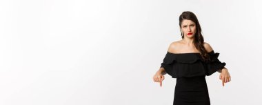 Moda ve güzellik. Hoşnutsuz bir kadın şikayet ediyor, kaşlarını çatıyor ve kötü şeyleri işaret ediyor, hayal kırıklıklarını ve hoşnutsuzluklarını dile getiriyor, beyaz arka plan.