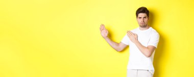 Kung-fu becerileri, dövüş sanatları ninja hareketi gösteren beyaz tişörtlü, savaşmaya hazır sarı arka planda duran bir adam. Boşluğu kopyala