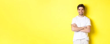 Kendinden emin, gülümseyen beyaz adamın görüntüsü mutlu, el ele tutuşmuş ve memnun görünüyor, sarı arka planda duruyor..