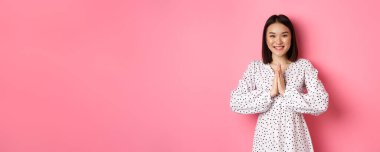 Güzel Asyalı kadın teşekkür ediyor. Takdir jesti olarak el ele tutuşuyor. Kameraya mutlu bir şekilde gülümsüyor..