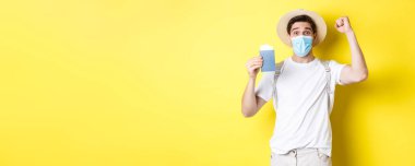 Covid-19 konsepti, seyahat ve karantina. Sağlık maskeli mutlu bir turist, tatil biletleri ve sevinçle pasaportunu gösteriyor, Coronavirus sırasında seyahat ediyor..