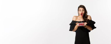 Kutlama ve parti konsepti. Doğum günü pastasında mum üfleyen, dilek tutan, siyah elbise giyen ve beyaz arka plana karşı makyaj yapan mutlu kadın..