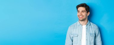 Genç, sakallı, sola bakan, gülümseyen, fotokopi alanından memnun, mavi arka planda duran.