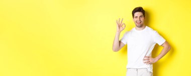 Kendine güveni olan yakışıklı bir adam göz kırpıyor. Onayladığına dair bir işaret veriyor. Sarı arka planda duran iyi bir şey gibi..