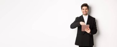 Siyah takım elbiseli yakışıklı bir girişimcinin portresi dijital tableti işaret ediyor, internette bir şey gösteriyor, beyaz arkaplana karşı duruyor..