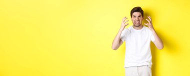 Kızgın adam kızgın görünüyor, somurtuyor ve tokalaşıyor öfkeli, sarı arka plana karşı öfkeli duruyor..