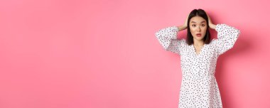 Şaşırmış ve sorunlu Asyalı kadın kafası karışmış görünüyor, el ele tutuşuyor, sorun yaşıyor, pembe arka planda duruyor..