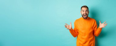 Mutlu ve heyecanlı adamın görüntüsü büyük haberleri duyurur, ellerini açar ve sevinç çığlıkları atar, neşe içinde, açık mavi arka planda durur..