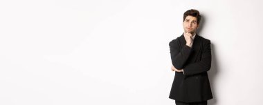 Takım elbiseli yakışıklı ve şık bir adamın portresi sol üst köşede düşünüyor ve bakıyor, Noel tatilleri hakkında bir şeyler hayal ediyor, beyaz arka planda duruyor..