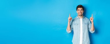 Sıradan giyinmiş yakışıklı bir adamın portresi. Mavi arka planda pankartı gösteriyor ve parmaklarını havaya kaldırıyor..