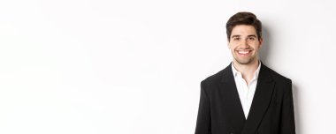 Yakından bakınca şık takım elbiseli yakışıklı genç iş adamı gülümsüyor, beyaz arka planda duruyor..