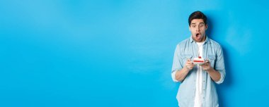 Doğum günü pastasına şaşırmış, mavi arka planda duran bir adam..