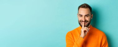 Yakışıklı, gülümseyen, sessiz, sırlarını açıklayan, açık mavi arka planda duran adamın yakın çekimi..