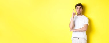 Düşünceli adam çözüm öneriyor, Eureka işaretinde parmağını kaldırıyor ve heyecanlı görünüyor, sarı arka plana karşı duran bir fikri var..