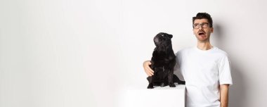 Sızlanan adam üzgün görünüyor, pug ise sol üst köşede, beyaz arka planda dikiliyor..