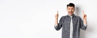 Heyecanlı yakışıklı adam parmak kaldırıyor, gülümsüyor, mutlu ve özel bir anlaşma yapıyor, beyaz arka planda duruyor..