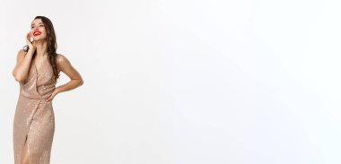 Parti ve kutlama konsepti. Zarif elbiseli, uzun boylu, mükemmel bir kadın. Gülüyor, Noel hediyelerinin yanında duruyor, beyaz bir arka plan..