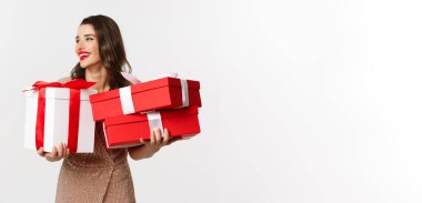 Tatiller, kutlama konsepti. Zarif elbiseli güzel beyaz kadın Noel hediyeleri taşıyor ve gülümsüyor, beyaz arka planda duruyor..