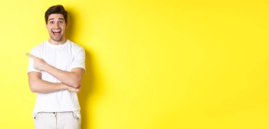 Mutlu adam solu işaret ediyor, fotokopi alanının reklamını yapıyor, gülümsüyor, beyaz elbiseler içinde sarı arka plana karşı duruyor..