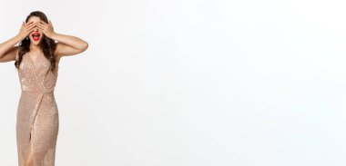 Parti ve kutlama konsepti. Kırmızı dudaklı, uzun boylu, alımlı bir kadın, Noel hediyelerinin yanında duruyor, gözlerini kapatıyor ve sürpriz bekliyor, beyaz arka plan.