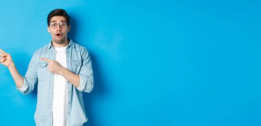 Gözlüklü şaşırmış bir adam fotokopi alanını işaret ediyor, ürün hakkında sorular soruyor, ilgi çekici görünüyor, mavi arka planda duruyor..