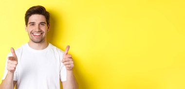 Kendine güvenen adam kamerayı işaret ediyor ve gülümsüyor, seni övüyor, sarı arka planda duruyor..