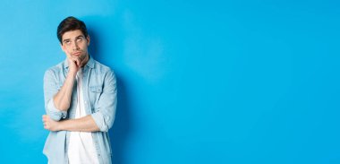 Kızgın yetişkin bir adam gözlerini deviriyor ve sıkılmış görünüyor. Sıradan kıyafetlerle mavi arka plana karşı kayıtsız kalıyor..