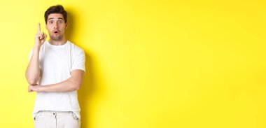 Düşünceli adam çözüm öneriyor, Eureka işaretinde parmağını kaldırıyor ve heyecanlı görünüyor, sarı arka plana karşı duran bir fikri var..