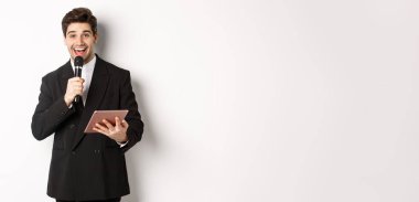 Yakışıklı bir erkek oyuncunun görüntüsü, konuşma yapması, insanları partide eğlendirmesi, mikrofon ve dijital tablet tutması, beyaz arka planda durması..