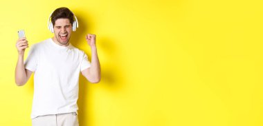 Mutlu adam dans ediyor ve kulaklıkla müzik dinliyor, cep telefonu tutuyor, sarı arka planda duruyor..