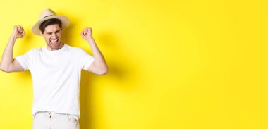 Turizm ve tatil kavramı. Mutlu adam seviniyor, bir şey kazanıyor ya da amacına ulaşıyor, sarı arka plana karşı zafer kazanıyor..