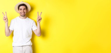 Turizm ve tatil kavramı. Barış işaretleriyle poz veren mutlu erkek turist, heyecanla gülümsüyor, sarı arka planda duruyor..